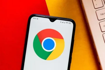 “Smartphone displaying the Google Chrome logo on screen, placed against a red and yellow background next to a laptop keyboard.”