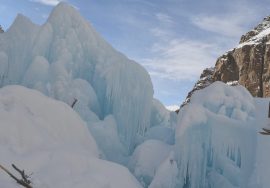 A large section of the Ulter Glacier in Hunza Valley showing massive blue ice formations and snow-covered surfaces between steep rocky mountains.