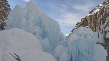 A large section of the Ulter Glacier in Hunza Valley showing massive blue ice formations and snow-covered surfaces between steep rocky mountains.