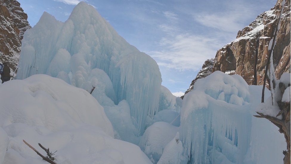 A large section of the Ulter Glacier in Hunza Valley showing massive blue ice formations and snow-covered surfaces between steep rocky mountains.