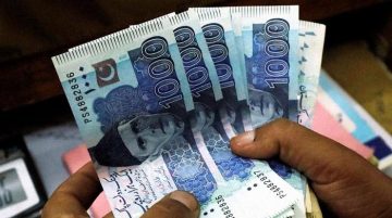 A person holding multiple 1000-rupee Pakistani banknotes fanned out in their hand.