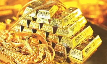 A stack of gold bars surrounded by gold jewelry under bright reflective lighting.
