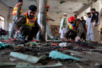 Rescue workers and police officers examine debris inside a damaged building after a violent attack, searching for evidence among burnt and scattered materials.