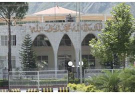A government building in Azad Jammu and Kashmir with an arched entrance and greenery in the foreground.