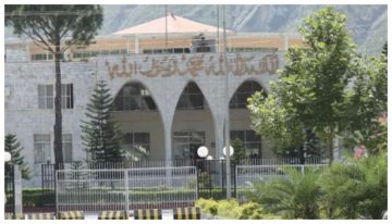 A government building in Azad Jammu and Kashmir with an arched entrance and greenery in the foreground.