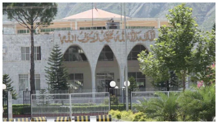 A government building in Azad Jammu and Kashmir with an arched entrance and greenery in the foreground.