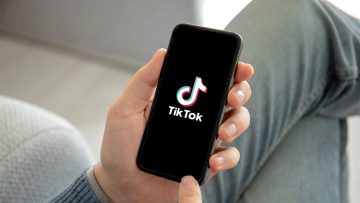 A person holding a smartphone displaying the TikTok logo on the screen.