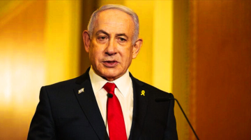 Israeli Prime Minister Benjamin Netanyahu speaking at a podium during an official address, wearing a black suit, red tie, and a yellow ribbon pin.
