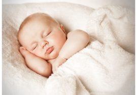 A peacefully sleeping baby wrapped in a soft white blanket, resting with one hand under the cheek.
