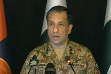 A Pakistani military spokesperson, Lieutenant General Ahmed Sharif, delivering an official press briefing at a podium with microphones. The backdrop shows Pakistan Army flags and branding. The screen displays a breaking news headline summarizing his statement about Pakistan targeting only terrorists and never civilians.