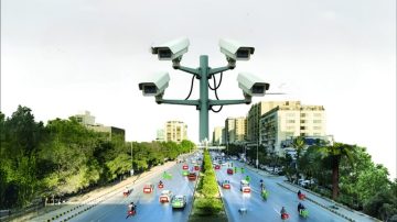 Traffic surveillance cameras monitoring vehicles on a busy Karachi road from an elevated central pole.