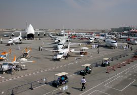 Various military and commercial aircraft displayed at the Dubai Airshow, with visitors walking around the exhibition area.
