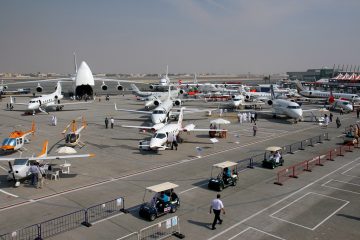 Various military and commercial aircraft displayed at the Dubai Airshow, with visitors walking around the exhibition area.