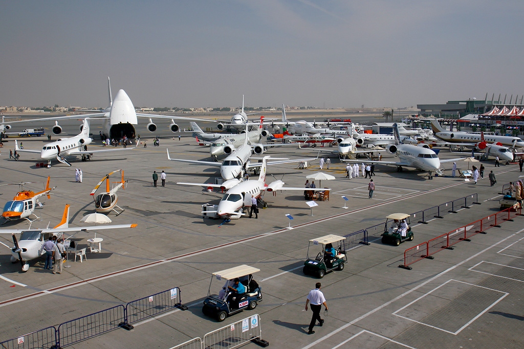 Various military and commercial aircraft displayed at the Dubai Airshow, with visitors walking around the exhibition area.