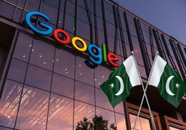 A photo of the Google corporate building with large colorful Google logo on glass windows during sunset. In front, two crossed Pakistani flags are placed, symbolizing Google’s official entry and upcoming office launch in Pakistan.