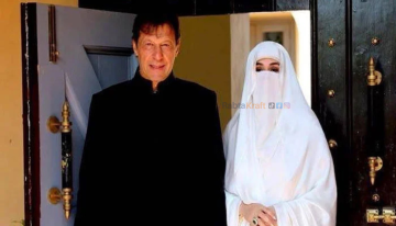 “Two people standing together at the entrance of a house; the man dressed in black traditional attire and the woman dressed in a full white veil, photo branded with RabtaKraft watermark.”