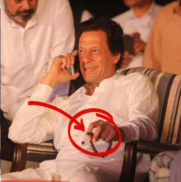 Imran Khan smiling while holding prayer beads during a phone call in a public gathering.