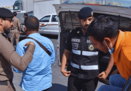 Saudi police officers detain and escort several individuals during a crackdown on illegal expatriates, with detainees being moved toward a police vehicle.