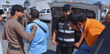 Saudi police officers detain and escort several individuals during a crackdown on illegal expatriates, with detainees being moved toward a police vehicle.