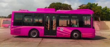 Pink public transport bus parked in Karachi depot under cloudy sky.