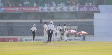 Cricketers and umpires stand in the middle of the field during the Bangladesh vs Ireland Test match as play is halted due to earthquake tremors. The stadium seats in the background appear partially empty, and sunlight falls across the ground.