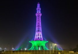 Minar-e-Pakistan illuminated at night with vibrant green and purple lights, showcasing the landmark’s architectural beauty.