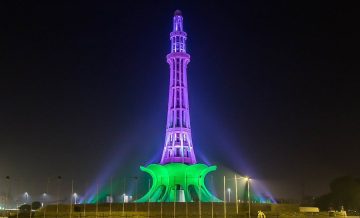 Minar-e-Pakistan illuminated at night with vibrant green and purple lights, showcasing the landmark’s architectural beauty.