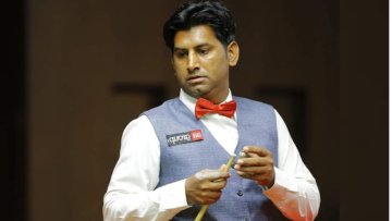 Pakistani snooker player Asjad Iqbal holding a cue stick during a professional snooker match, wearing a waistcoat and red bow tie.