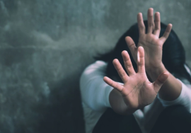 A distressed young woman raising her hands to protect herself from assault, symbolizing violence and abuse against women.