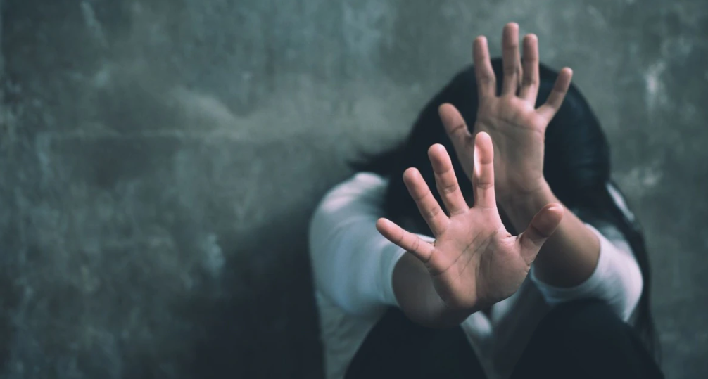 A distressed young woman raising her hands to protect herself from assault, symbolizing violence and abuse against women.