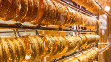 Rows of gold bangles displayed on multiple racks inside a jewelry shop, showcasing intricate designs and bright golden shine.