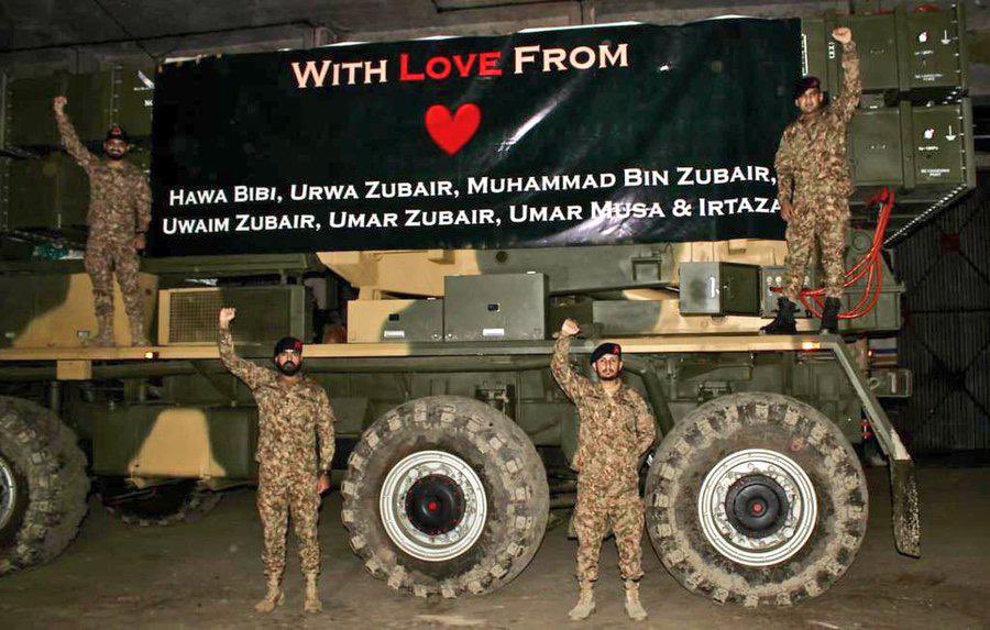 Pak Army ke chand faujis ek bade military vehicle par kharay hain. Vehicle ke upar ek bari black banner lagi hai jisper “With Love From” likha hua hai aur neeche kuch naam list kiye gaye hain. Faujis haath buland kar ke pose de rahe hain aur background aik andhera warehouse ya shed lag raha ha