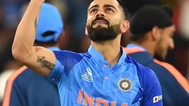 An Indian cricketer in a blue India jersey raises one finger toward the sky while looking upward, celebrating on the field.