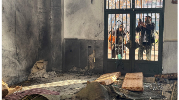Interior of a mosque in Homs, Syria showing damage and debris after an explosion during Friday prayers, as security personnel stand outside