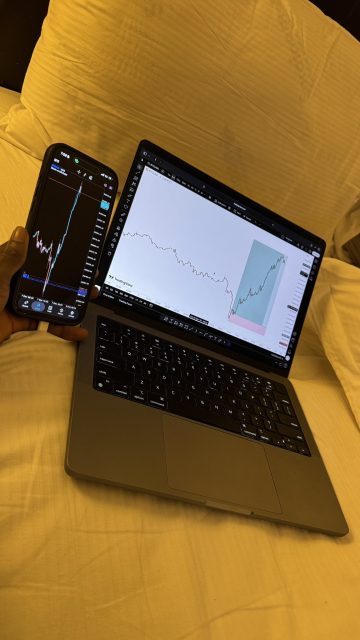“Smartphone and laptop showing trading charts on a bed.”