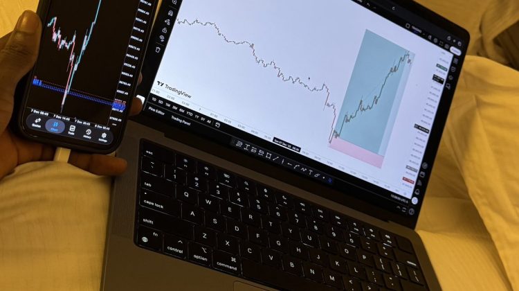 “Smartphone and laptop showing trading charts on a bed.”