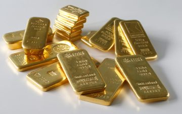 A collection of shiny gold bars of various sizes stacked and scattered on a white surface, each bar stamped with weight, purity, and refinery markings.