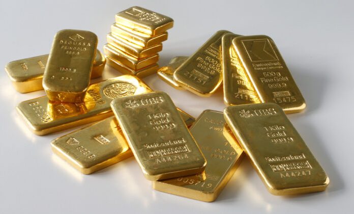 A collection of shiny gold bars of various sizes stacked and scattered on a white surface, each bar stamped with weight, purity, and refinery markings.