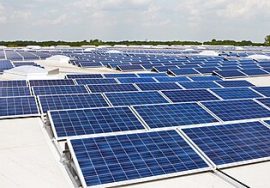 Rows of blue solar panels installed on a large flat rooftop under a bright sky, capturing sunlight for clean energy production.