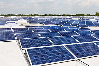 Rows of blue solar panels installed on a large flat rooftop under a bright sky, capturing sunlight for clean energy production.