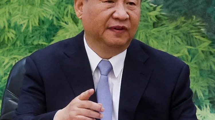 "A man in a formal suit speaking during a meeting, seated at a table with microphones in front of him."
