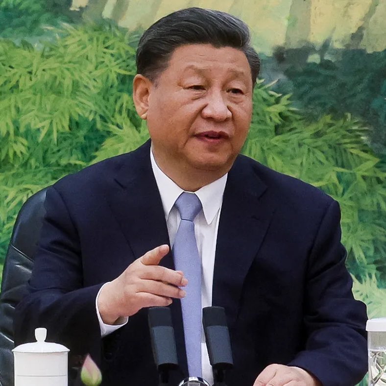 "A man in a formal suit speaking during a meeting, seated at a table with microphones in front of him."
