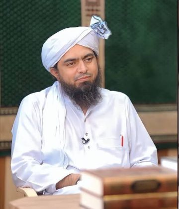 "A religious scholar wearing traditional white attire and a turban seated during a discussion program."
