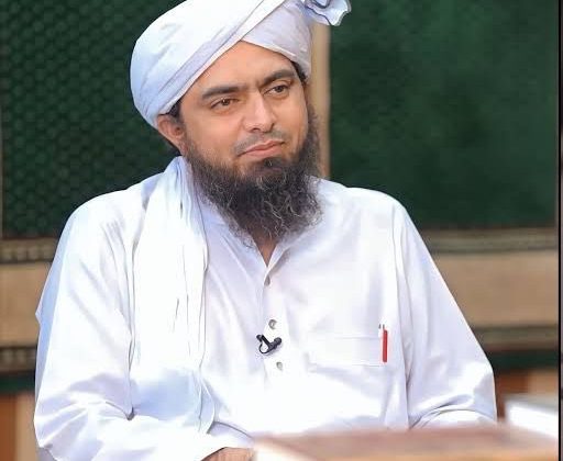 "A religious scholar wearing traditional white attire and a turban seated during a discussion program."