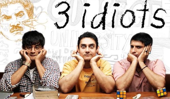 "Main cast of the Bollywood film 3 Idiots sitting at a desk with humorous expressions, featuring Aamir Khan, R. Madhavan, and Sharman Joshi."