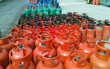 Rows of red, blue, and green LPG gas cylinders arranged outdoors in a storage area.