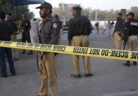 Police officers standing behind yellow crime-scene tape at a sealed-off area during an investigation.
