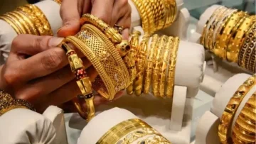 A close-up view of multiple gold bangles displayed in a jewelry shop, with a person’s hand selecting one of the intricate gold pieces.