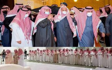 A group of Saudi men wearing traditional attire—thobes and red-and-white checkered shemaghs—carrying a coffin during a funeral procession, while a larger gathering stands in prayer in the background.