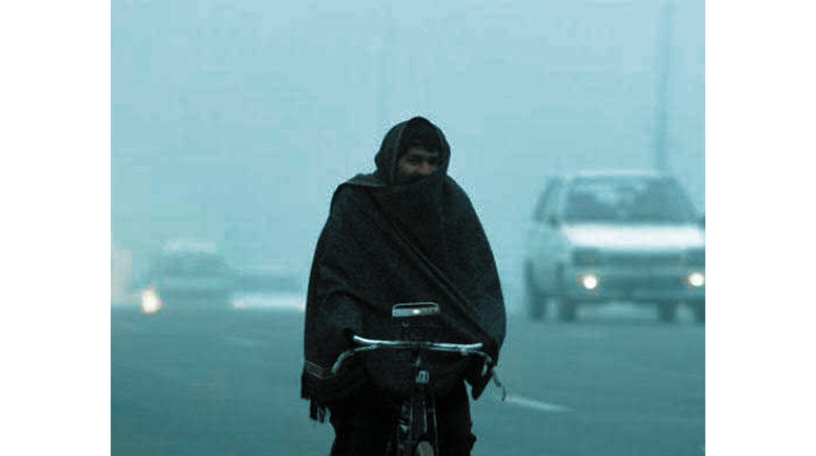 A man riding a bicycle in cold foggy weather, wrapped in a shawl during winter conditions